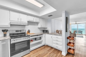 Une cuisine moderne avec des meubles blancs, des appareils en acier inoxydable et une vue sur l’extérieur.