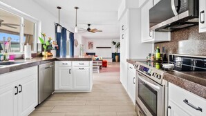 Une cuisine moderne avec des meubles blancs, un four à micro-ondes, un four traditionnel et un ventilateur de plafond.