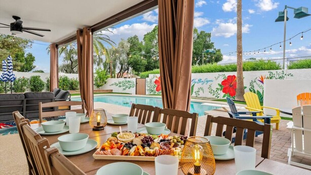 Un espace repas extérieur avec vue sur la piscine, doté de mobilier en bois et d’une table dressée avec un assortiment de fruits.