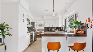 Une cuisine moderne avec des meubles blancs, un îlot central doté de tabourets de bar et une vue sur l’espace repas.