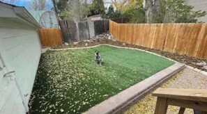 Ein Garten mit Holzterrasse, umzäuntem Bereich und Rasenfläche.