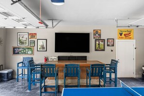 Una habitación con una televisión de pantalla plana grande, cuadros en las paredes, una mesa de ping pong y una puerta con el letrero de Vienna Beef.