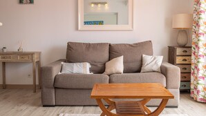 Una sala de estar con un sofá, una mesa de centro de madera, una lámpara, un espejo y una cortina estampada con motivos florales.