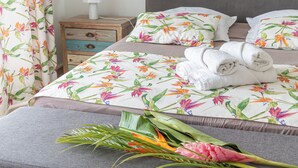 Una cama bien hecha con ropa de cama floral, una mesita de noche con lámpara y un mueble auxiliar con cajones.