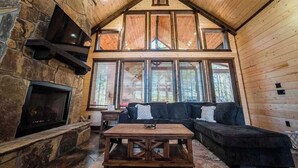 L’intérieur d’une cabane en rondins, avec une cheminée en pierre, un plafond en bois et de grandes fenêtres.