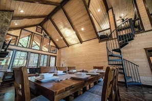Ein Holzinterieur mit Esstisch, Treppe und großen Fenstern.