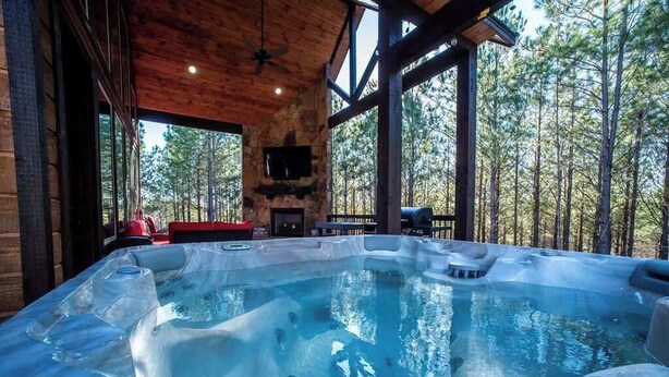 Un bain à remous dans un chalet en bois, avec une cheminée et une vue sur la forêt.