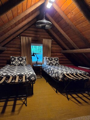 Un dormitorio en el ático con dos camas, un escritorio, una lámpara y una ventana con cortinas.