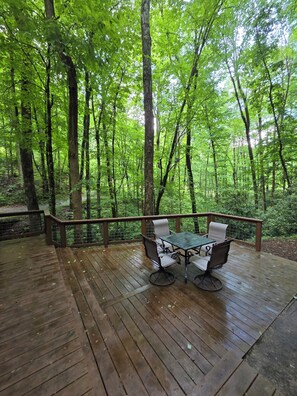 Una terraza de madera con una mesa y sillas, rodeada de un bosque.