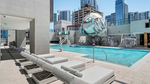 A rooftop pool with lounge chairs, a large glass building in the background, and a unique sculpture. - Luxury E11EVEN Studio 50th Floor with Elite Amenities (Miami)