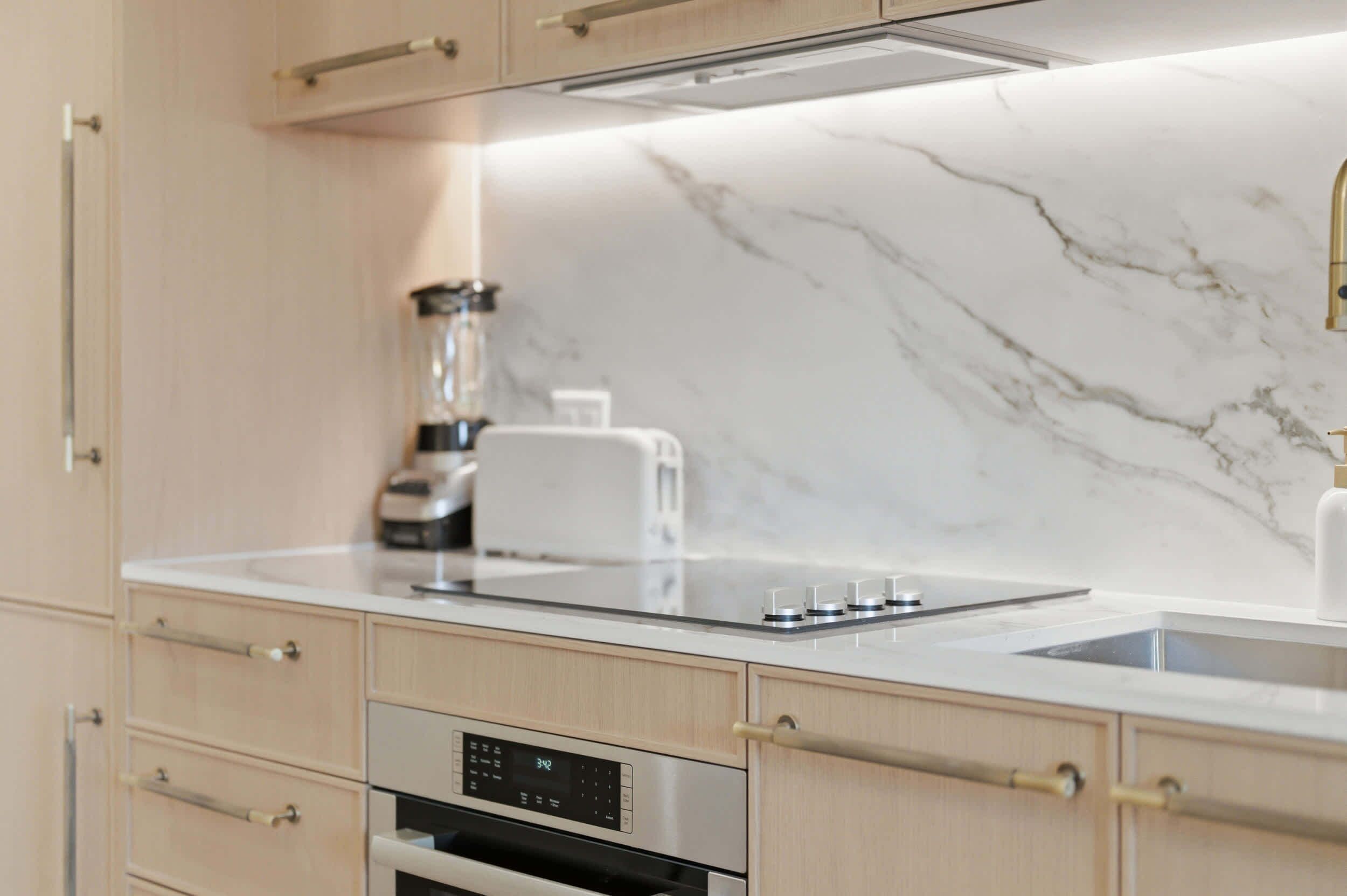A modern kitchen with a marble countertop, built-in oven, and a coffee maker.