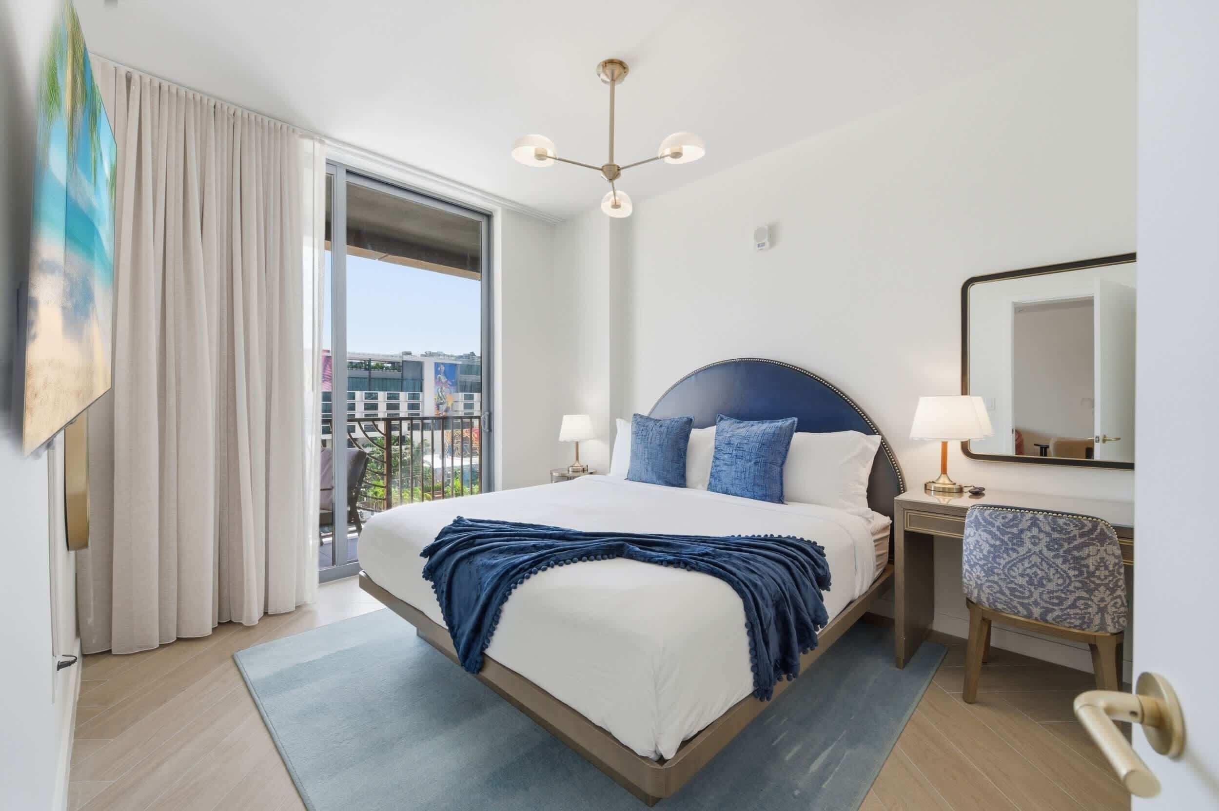Hotellihuone, jossa on sänky, työpöytä, tuoli, suuri ikkuna ja kattovalaisin.
