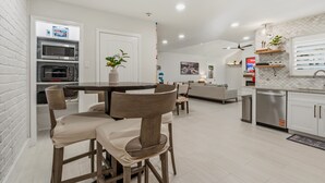 A modern kitchen with built-in appliances, a dining area with a round table and chairs, and a living space with a sofa and a TV. - Bean House Near NASA • Kemah Boardwalk • Galveston (Webster)