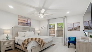 A bedroom with a bed, nightstands, a desk, a chair, a ceiling fan, and a window with curtains. - Bean House Near NASA • Kemah Boardwalk • Galveston (Webster)