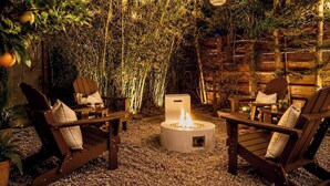 Un área de estar al aire libre con un brasero, sillas de madera y luces colgantes.