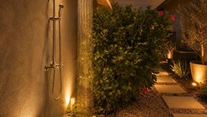 Una ducha exterior moderna con un chorro de agua vertical, una manguera fijada a la pared y una llave de control.