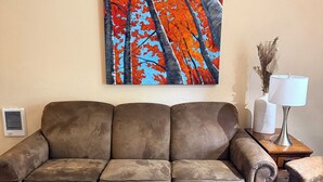 A living room with a brown sofa, a wooden coffee table, and a painting of trees on the wall.