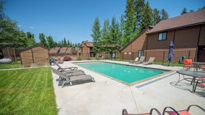 A swimming pool with lounge chairs, a covered patio area, and a fenced yard with trees.