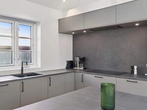 A modern kitchen with grey cabinets, a stainless steel sink, a coffee maker, and a green vase on the counter.