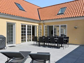 An outdoor patio with a tiled roof, open doors leading to a covered area, and a grill.
