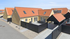 Una fila de casas modernas con tejados de tejas anaranjadas, un patio con muebles de exterior y un cielo despejado.
