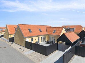 A row of modern houses with orange tiled roofs, a patio area with outdoor furniture, and a clear sky.
