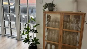Una habitación con puerta corredera de vidrio, una planta en maceta, un mueble de madera con puertas de cristal y una lámpara de pie.