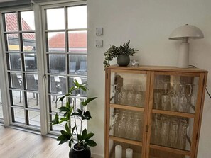 A room with a sliding glass door, a potted plant, a wooden cabinet with glass doors, and a floor lamp.