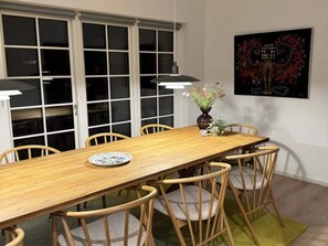 A dining room with a wooden table, six chairs, a vase with flowers, and a painting on the wall.