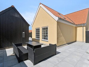 A building with a sloped roof, a patio with outdoor furniture, and a wooden structure to the left. - 4 Star Holiday Home in Skagen (Skagen)