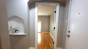 Un pasillo con suelo de madera, paredes blancas y una puerta blanca.