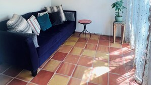 Een kamer met een donkerblauwe bank, een klein rond tafeltje, een potplant en een ingelijst schilderij aan de muur.