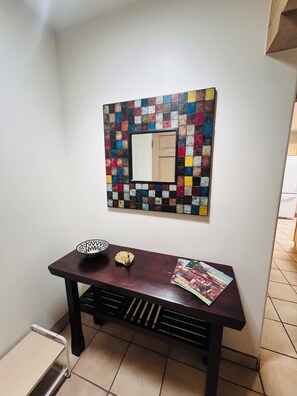 A hallway with a tiled wall, a mirror, a dark wooden table with a magazine, a decorative bowl, and a small white shelf. -  Sunny, Tranquil Two-Bedroom Home Near Santa Fe’s Best Attractions (Santa Fe)