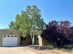 A building with a garage, a tree with green leaves, and a bush with red leaves.