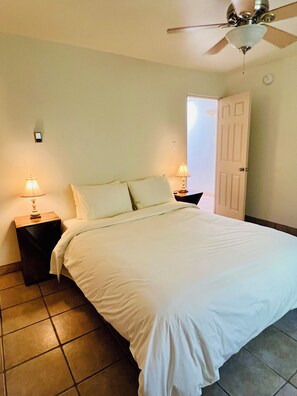 A bedroom with a bed, two bedside tables with lamps, a ceiling fan, and a door.