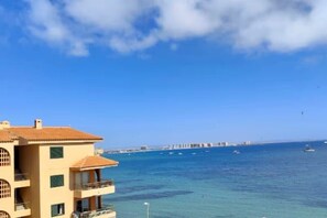 A multi-story building with balconies overlooking a clear blue sea, a pier in the distance, and a clear sky. - Beachfront 3BR Condo w/ Pool Views - Sleeps 10 (MC)
