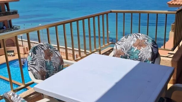 Un balcón con vista al mar, una piscina y una mesa con sillas.