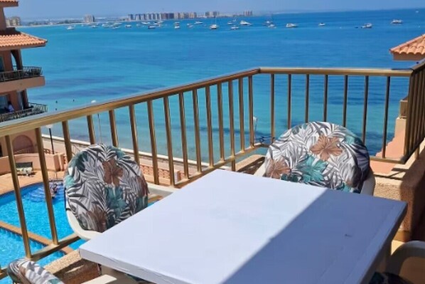 A balcony with a view of the sea, a pool, and a table with chairs. - Beachfront 3BR Condo w/ Pool Views - Sleeps 10 (MC)