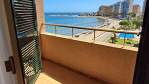 Un balcón con vistas a una playa, una piscina y edificios al fondo.