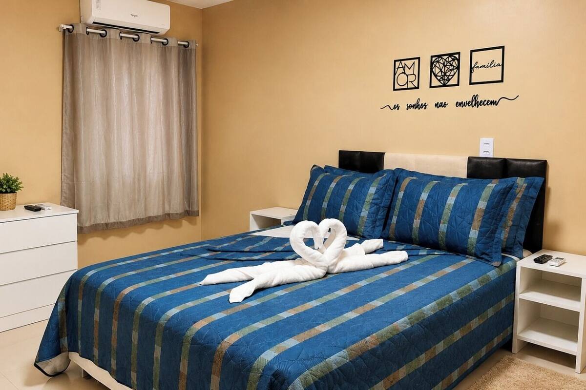 A hotel room with a bed, a nightstand, a dresser, a mirror, a wall with decorative items, and a window with curtains.