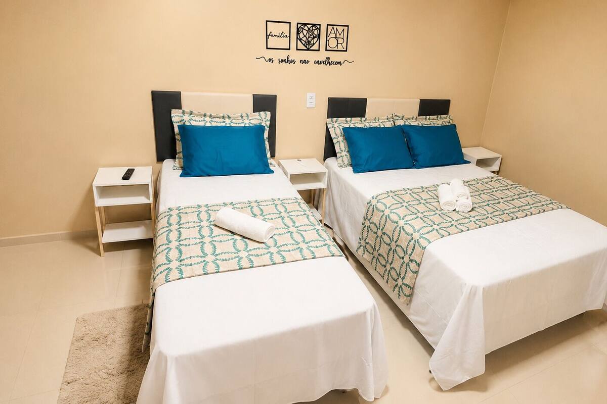 Two twin beds with matching headboards, white bedding, and blue pillows in a room with a beige wall and a small rug.