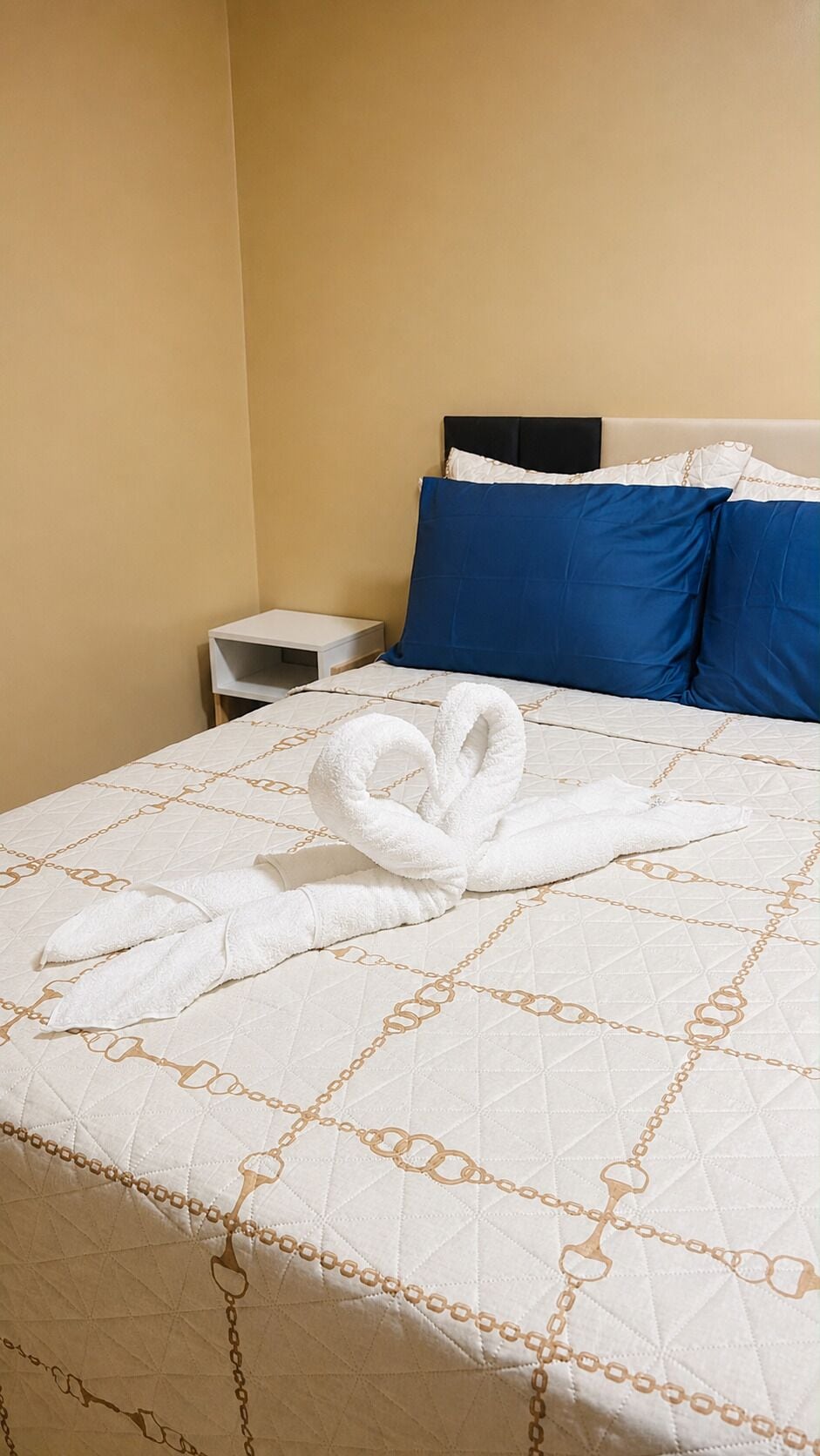 Una habitación de hotel con una cama, una mesita de noche y una almohada azul.