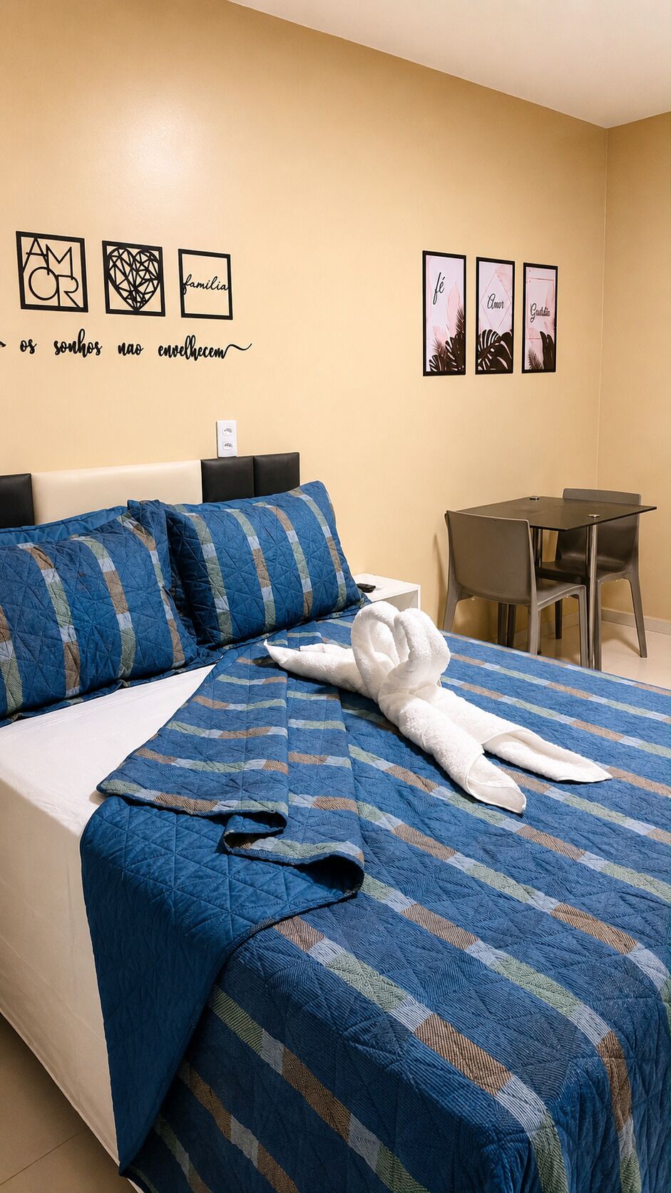 A hotel room with a bed, a desk, and a chair. There are wall decorations and a towel on the bed.