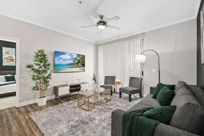 Een moderne woonkamer met een bank, stoelen, een salontafel, een televisie en een plafondventilator.