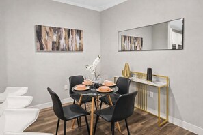 Een eetgedeelte met een ronde tafel, zwarte stoelen en een consoletafel met gouden lijst en een spiegel.