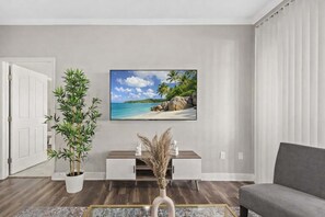 A living room with a large flat-screen TV mounted on the wall, a potted plant, a console table with decorative items, and a grey sofa. - Scottsdale Serenity | Pools, Patio, Pets OK (Scottsdale)