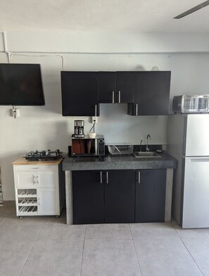 Eine kleine Küche mit schwarzen Schränken, einem weißen Kühlschrank, einer Kaffeemaschine und einem Toaster.
