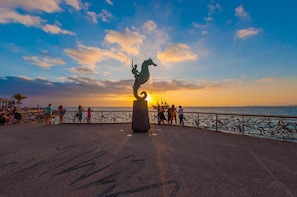 Eine Uferpromenade mit Skulptur, Menschen und Sonnenuntergang.