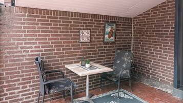 Un patio con paredes de ladrillo, una mesa, dos sillas, una alfombra pequeña y un cartel en la pared.