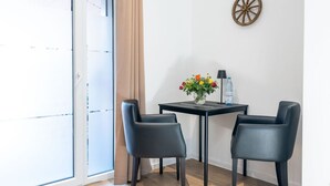 Een kamer met een schuifglasraam, een klein tafeltje met stoelen, een vaas met bloemen en een waterfles.